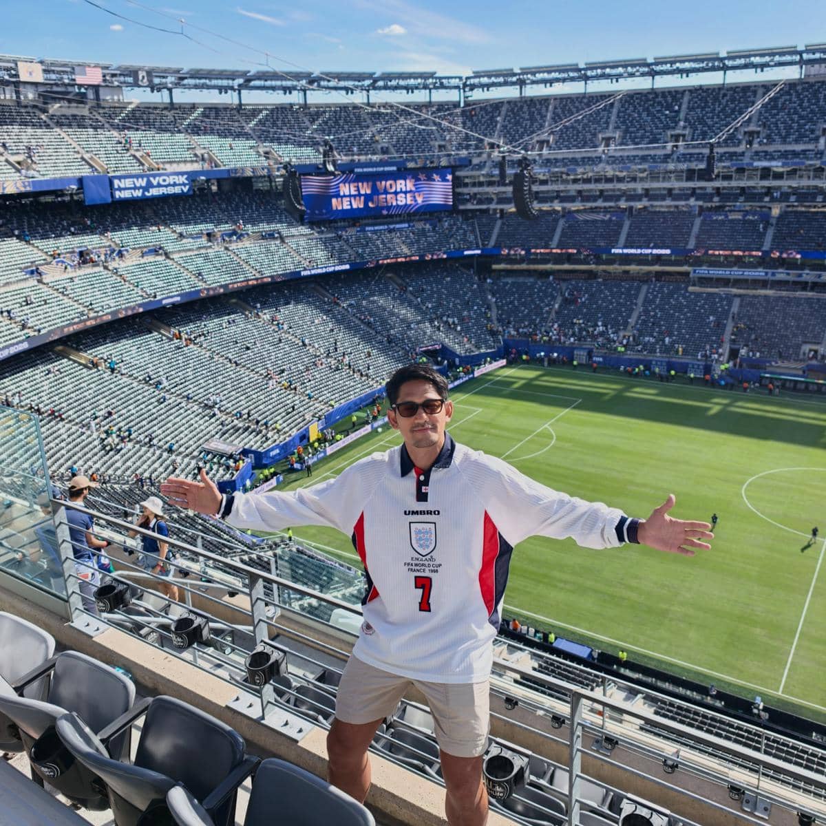 Seorang pria mengenakan jersey timnas Inggris berdiri di tribun stadion sepak bola di New York New Jersey dengan tangan terbuka lebar.