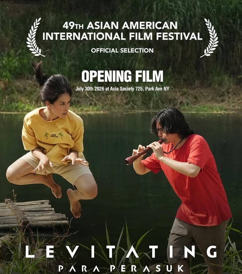 Dua aktor dalam adegan film Para Perasuk, satu melayang di udara sementara yang lain memainkan seruling di tepi sungai.