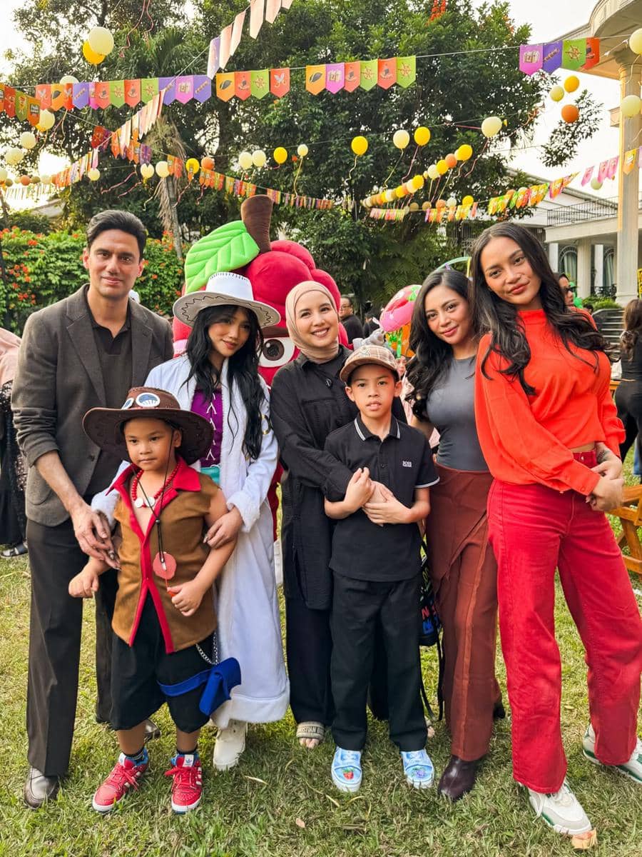 Sekelompok tamu berpose bersama anak-anak di pesta ulang tahun ke-6 Gala Sky dengan dekorasi balon dan bendera warna-warni di luar ruangan.