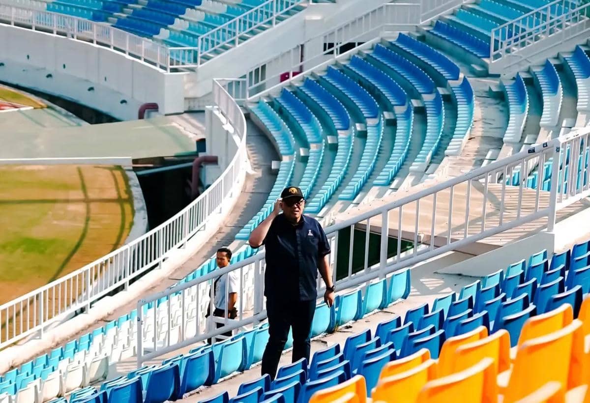 Seorang anggota tim verifikator berjalan di antara deretan kursi berwarna biru dan oranye di Stadion Kanjuruhan saat inspeksi berlangsung.