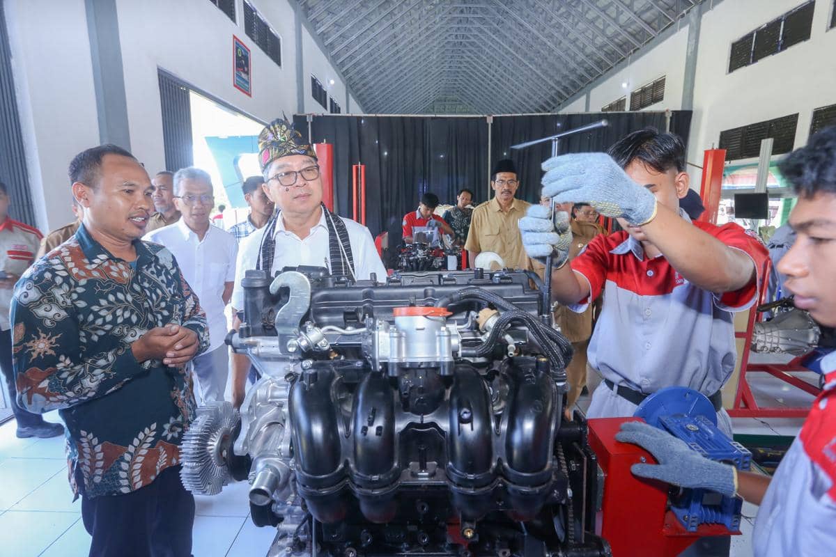 Siswa SMK mempraktikkan pembelajaran otomotif dengan mesin Toyota di bengkel sekolah, disaksikan oleh guru dan tamu.