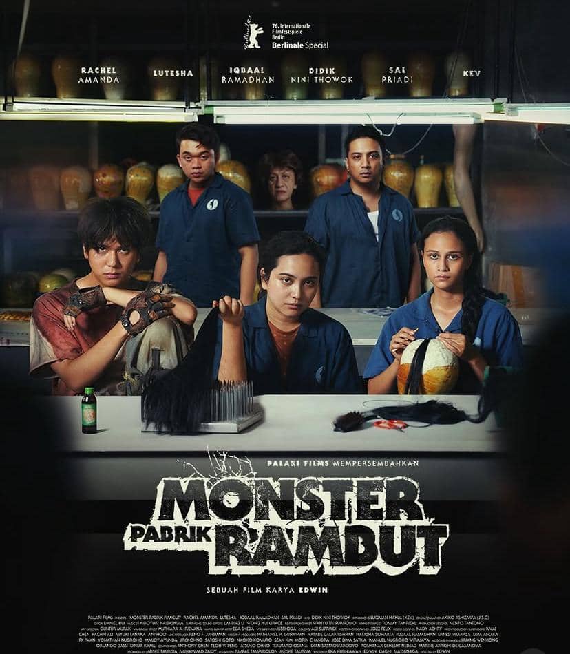 Poster film Monster Pabrik Rambut menampilkan beberapa pemeran utama duduk di meja kerja pabrik dengan alat dan rambut palsu di sekitarnya.