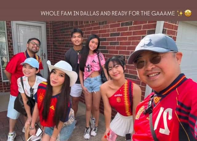 Sekelompok orang berpakaian kasual dan jersey sepak bola berfoto bersama di depan dinding bata sebelum menonton pertandingan Spanyol versus Prancis.