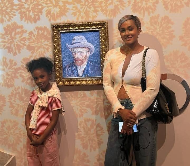 Seorang wanita dan anak perempuan berpose di depan lukisan potret Vincent van Gogh di Museum Van Gogh dengan latar dinding bermotif bunga.