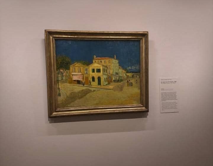 Lukisan pemandangan kota dengan bangunan kuning di dinding museum, dipajang dalam bingkai kayu di Museum Van Gogh.