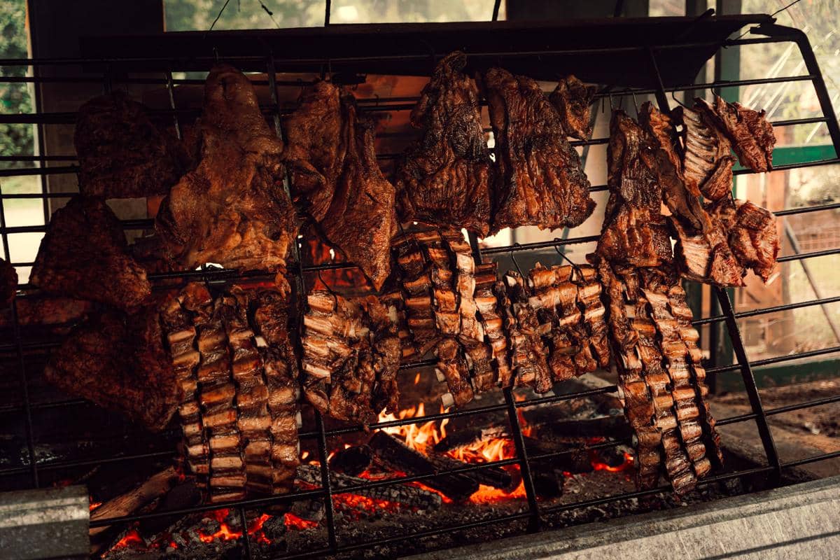 Potongan daging sapi dipanggang di atas bara api dengan teknik asado, menampilkan warna kecokelatan dan tekstur daging yang menggugah selera.
