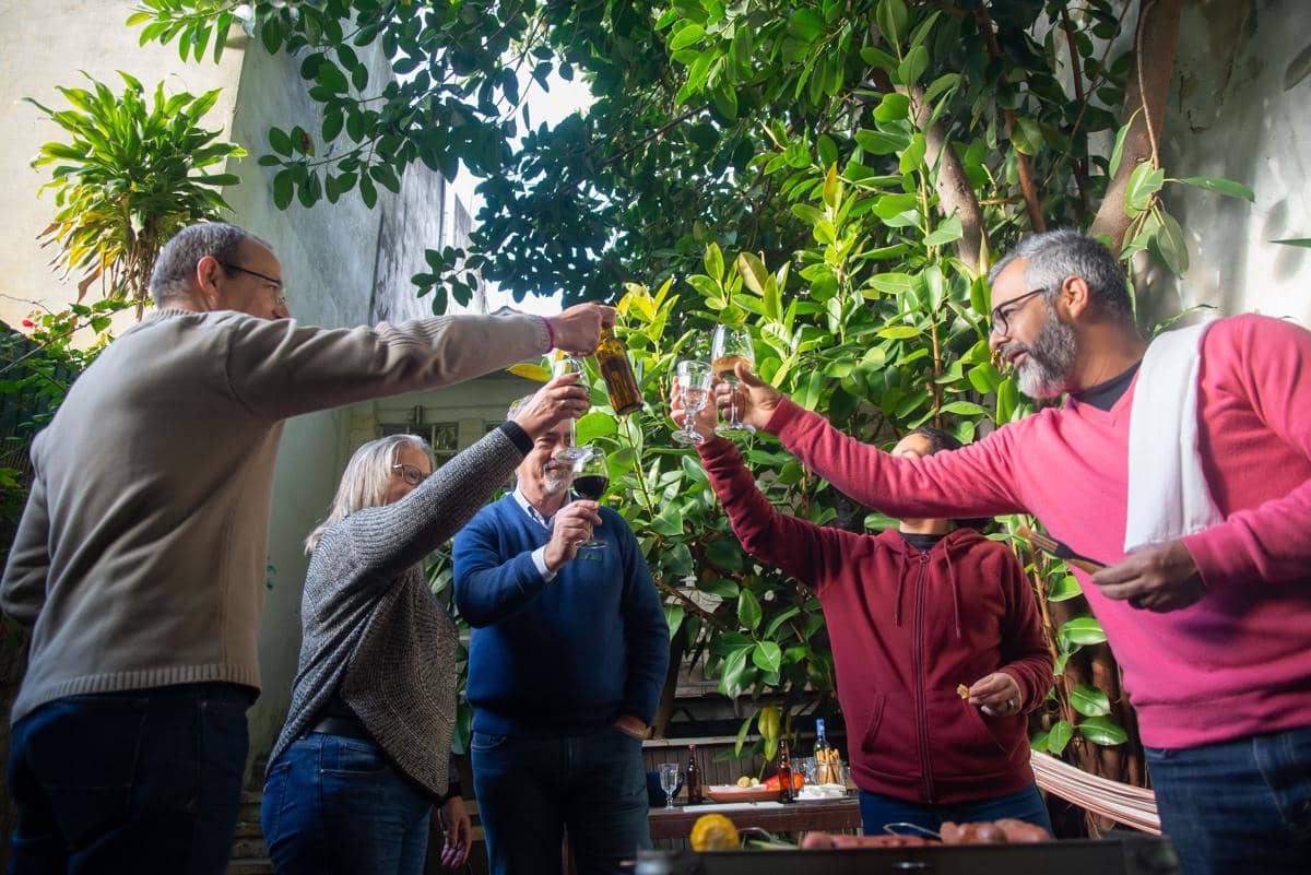 Sekelompok orang dewasa berkumpul di taman sambil bersulang dengan gelas minuman di tangan, dikelilingi pepohonan hijau.