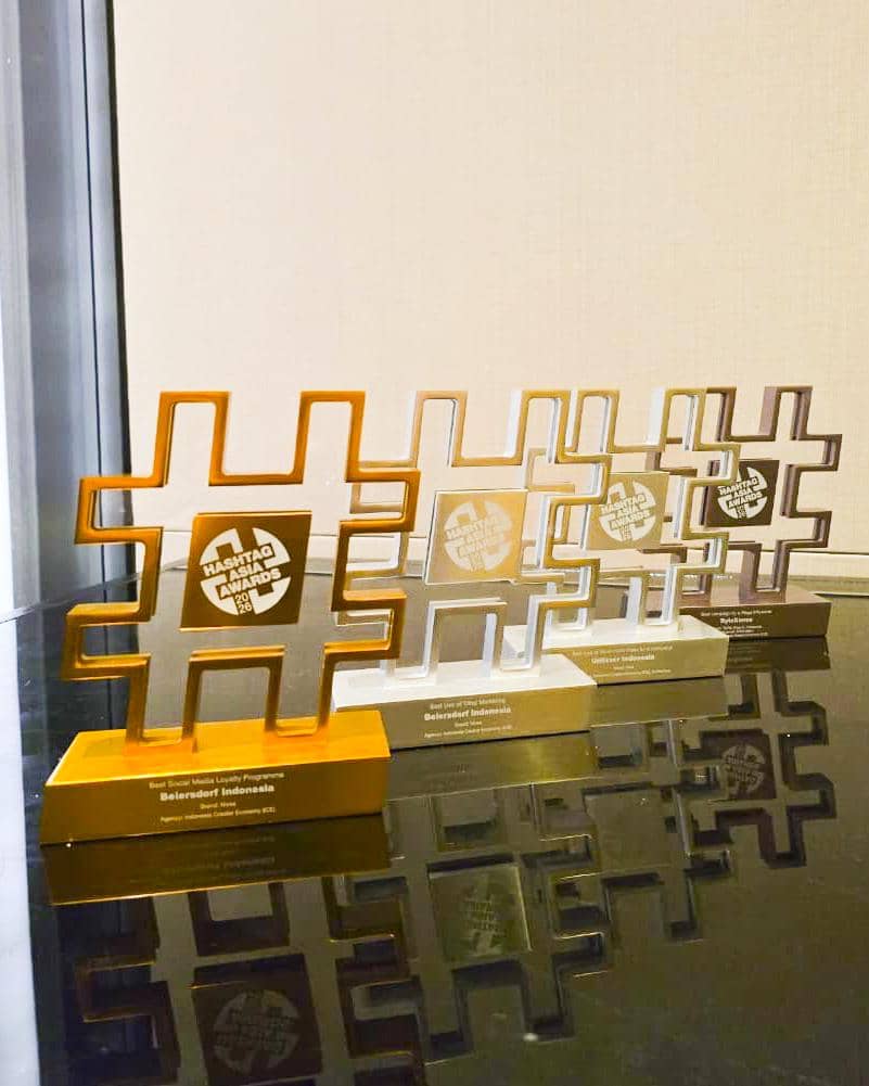 Empat trofi berbentuk simbol pagar dari Hashtag Asia Awards 2026 berwarna emas dan perak tersusun di atas meja kaca.
