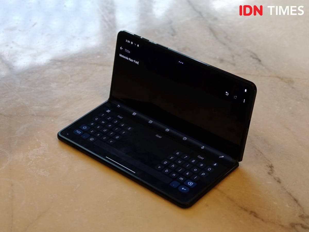 Ponsel lipat Motorola Razr Fold berwarna hitam terbuka sebagian di atas permukaan meja marmer dengan layar menampilkan keyboard virtual.
