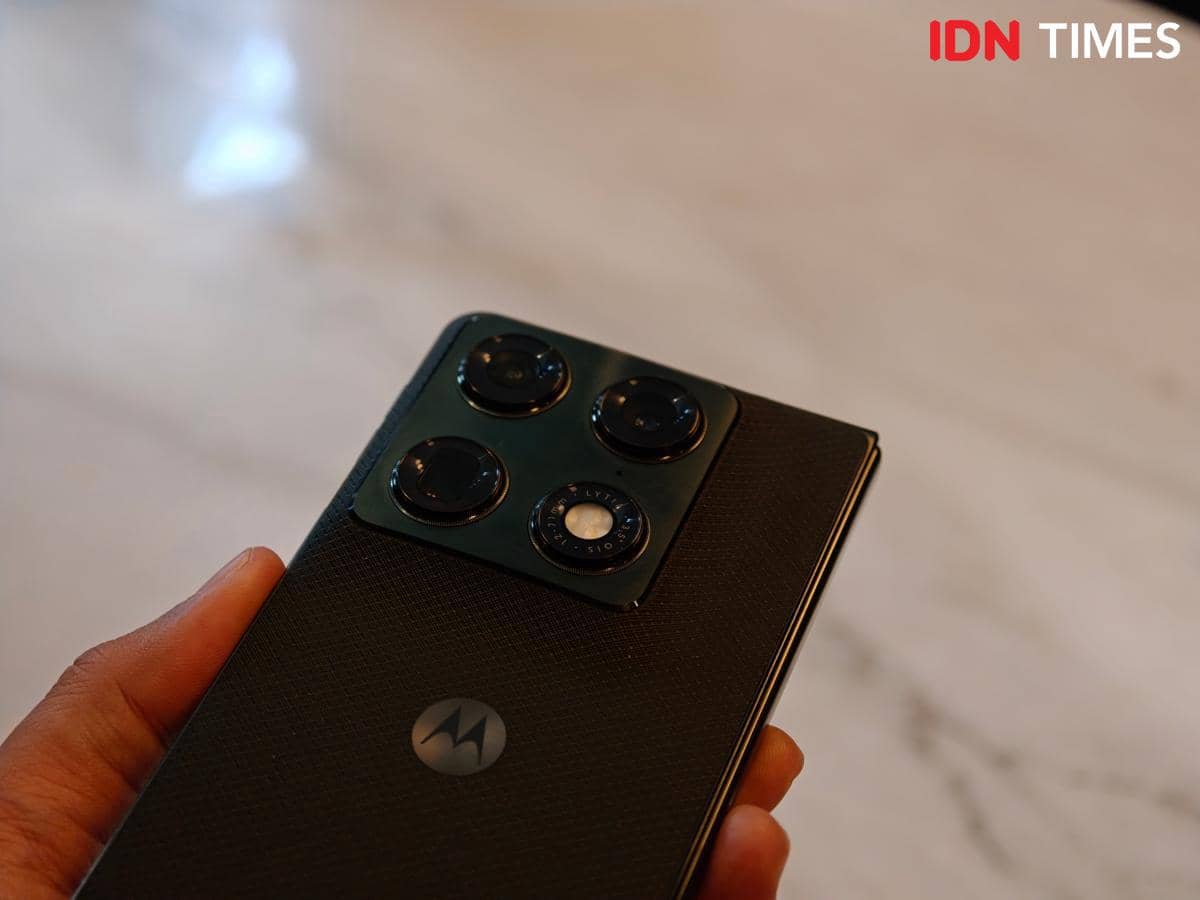 Seseorang memegang ponsel lipat Motorola Razr Fold berwarna hitam dengan empat kamera belakang di atas permukaan meja marmer.