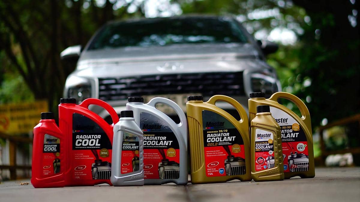 Deretan produk cairan radiator Master berbagai varian dan ukuran ditempatkan di depan mobil berwarna perak di area luar ruangan.