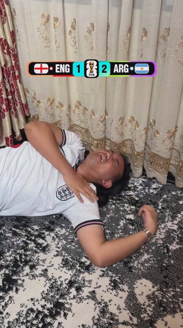 Seorang pria mengenakan kaus tim nasional Inggris berbaring di lantai sambil bereaksi emosional setelah kekalahan Inggris dari Argentina 1-2 di Piala Dunia 2026.