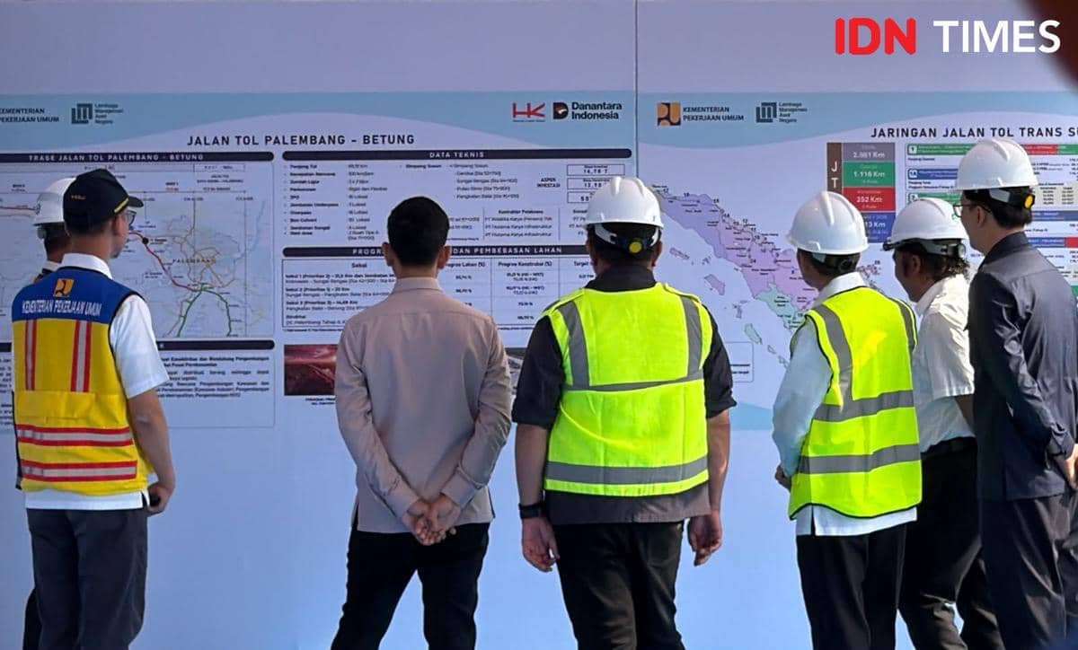 Beberapa orang mengenakan helm proyek dan rompi keselamatan melihat peta pembangunan Jalan Tol Palembang-Betung di area proyek.