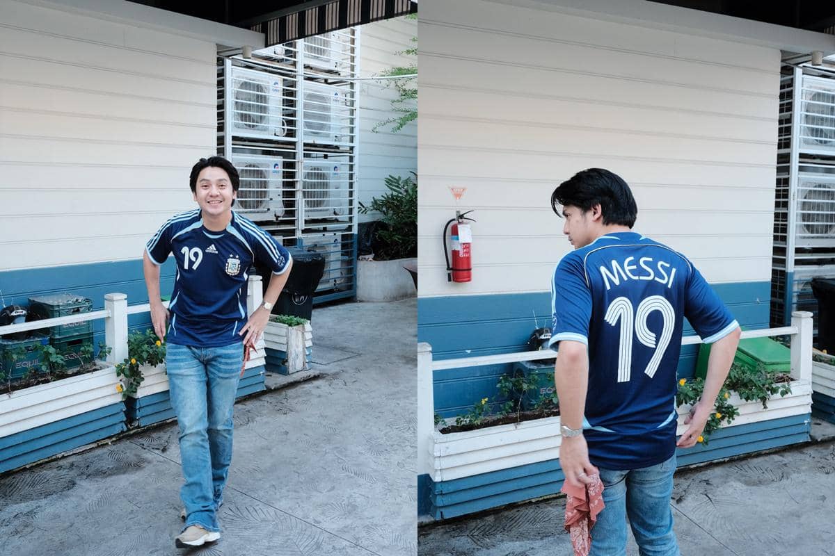Seorang pria mengenakan jersey tim nasional Argentina bernomor 19 dengan nama Messi, berpose santai di area luar bangunan.
