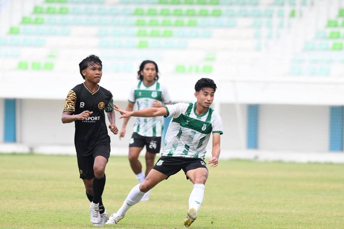 Pemain PSMS dan Muspika FC berebut bola dalam pertandingan di Stadion Min Pancing dengan latar tribun kosong berwarna hijau putih.
