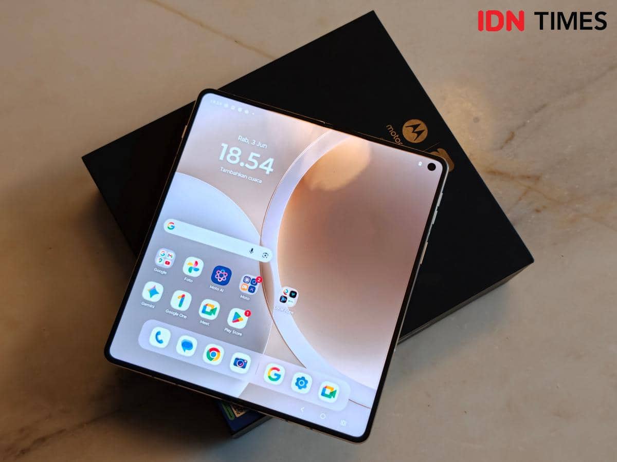 Smartphone lipat Motorola Razr Fold dengan layar terbuka menampilkan antarmuka utama di atas meja marmer bersama kotak kemasannya.