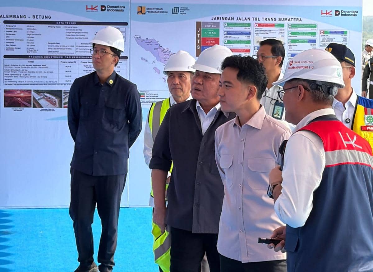 Beberapa pejabat mengenakan helm proyek meninjau pembangunan Jembatan Musi V di ruas tol Palembang-Betung dengan latar peta dan data teknis.