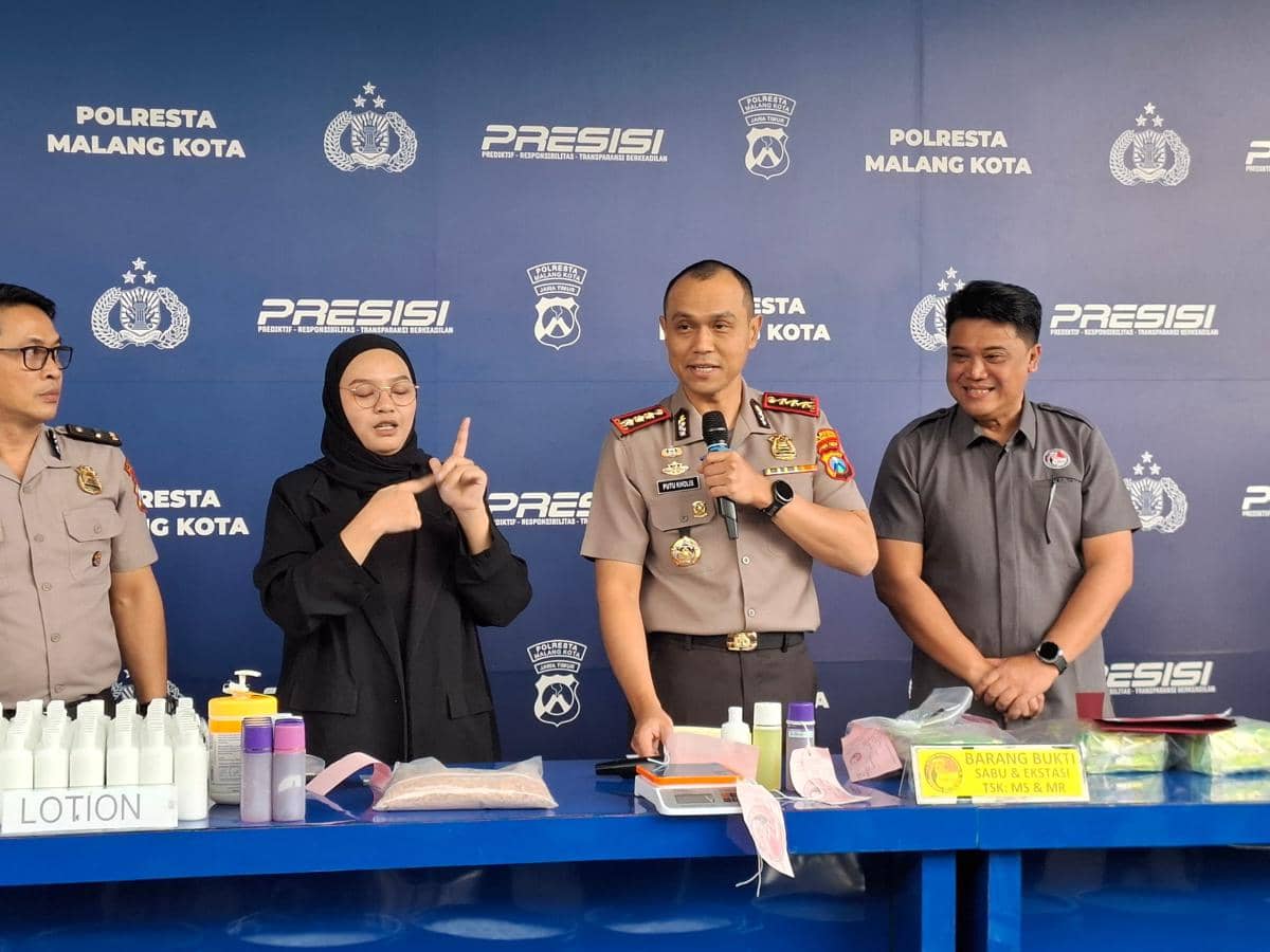 Kapolresta Malang Kota berbicara dalam konferensi pers bersama beberapa petugas dan juru bahasa isyarat di depan meja barang bukti.