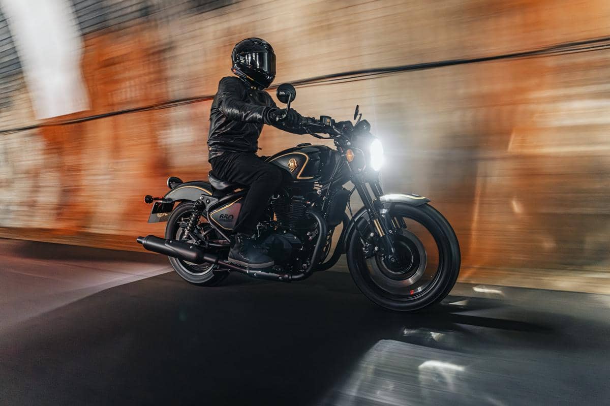Pengendara mengenakan jaket dan helm hitam mengendarai motor Royal Enfield Shotgun 650 x Rough Crafts Edition di dalam terowongan.