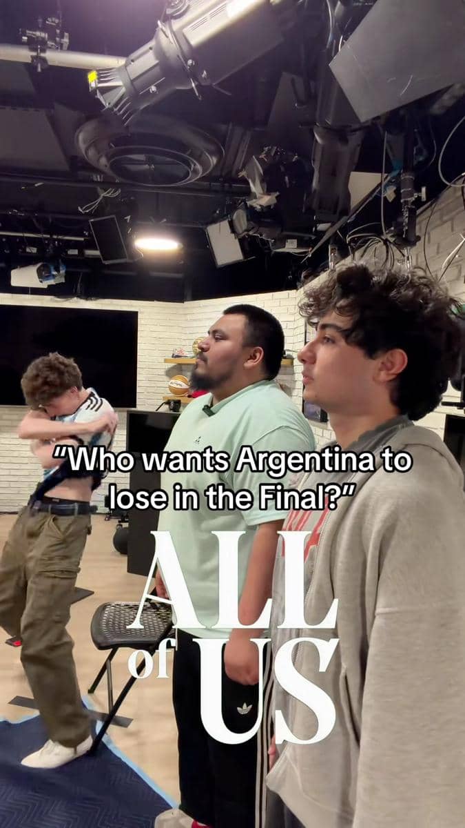 Tiga pria berdiri di dalam studio dengan pencahayaan profesional, salah satunya tampak bereaksi kuat terhadap pertanyaan tentang tim Argentina.