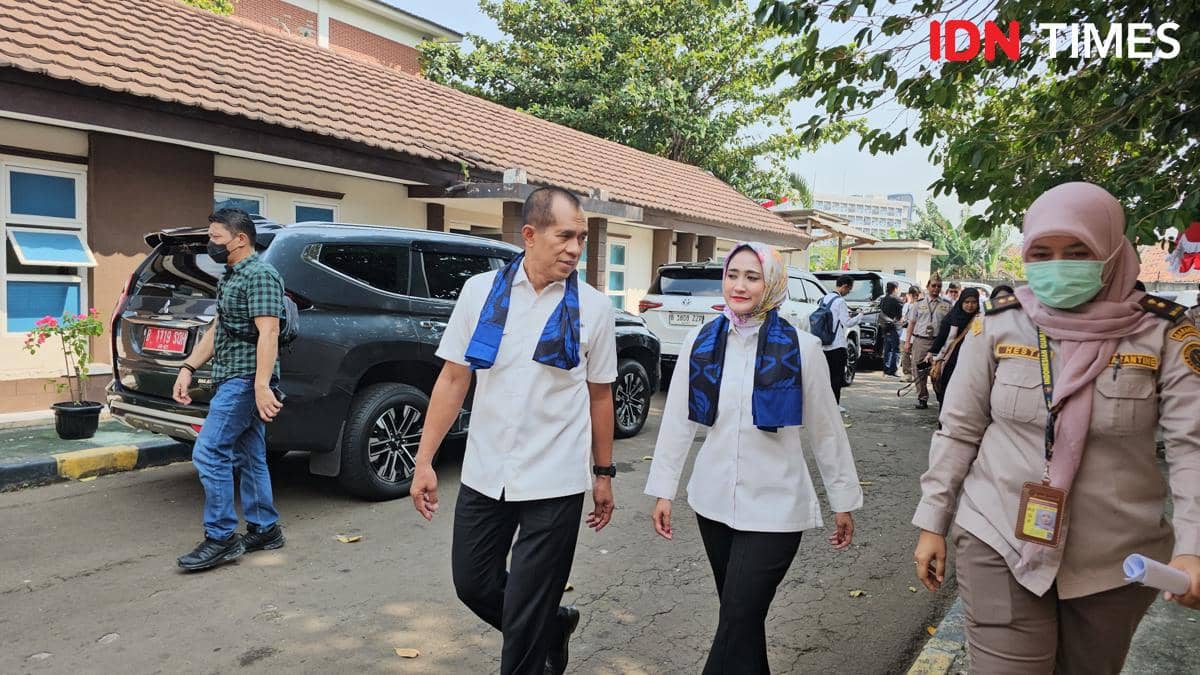 Anggota Komisi IV DPR RI berjalan bersama petugas karantina di area Satuan Layanan Karantina Soekarno-Hatta dengan latar gedung dan kendaraan dinas.
