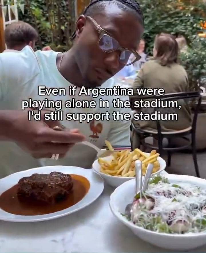 Seorang pria mengenakan kacamata sedang makan steak, kentang goreng, dan salad di restoran dengan teks meme tentang dukungan terhadap Argentina.