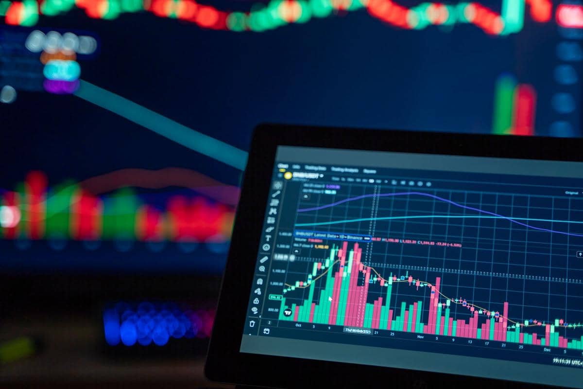 Grafik portofolio investasi dengan diagram batang dan garis berwarna di layar komputer yang menampilkan pergerakan pasar keuangan.