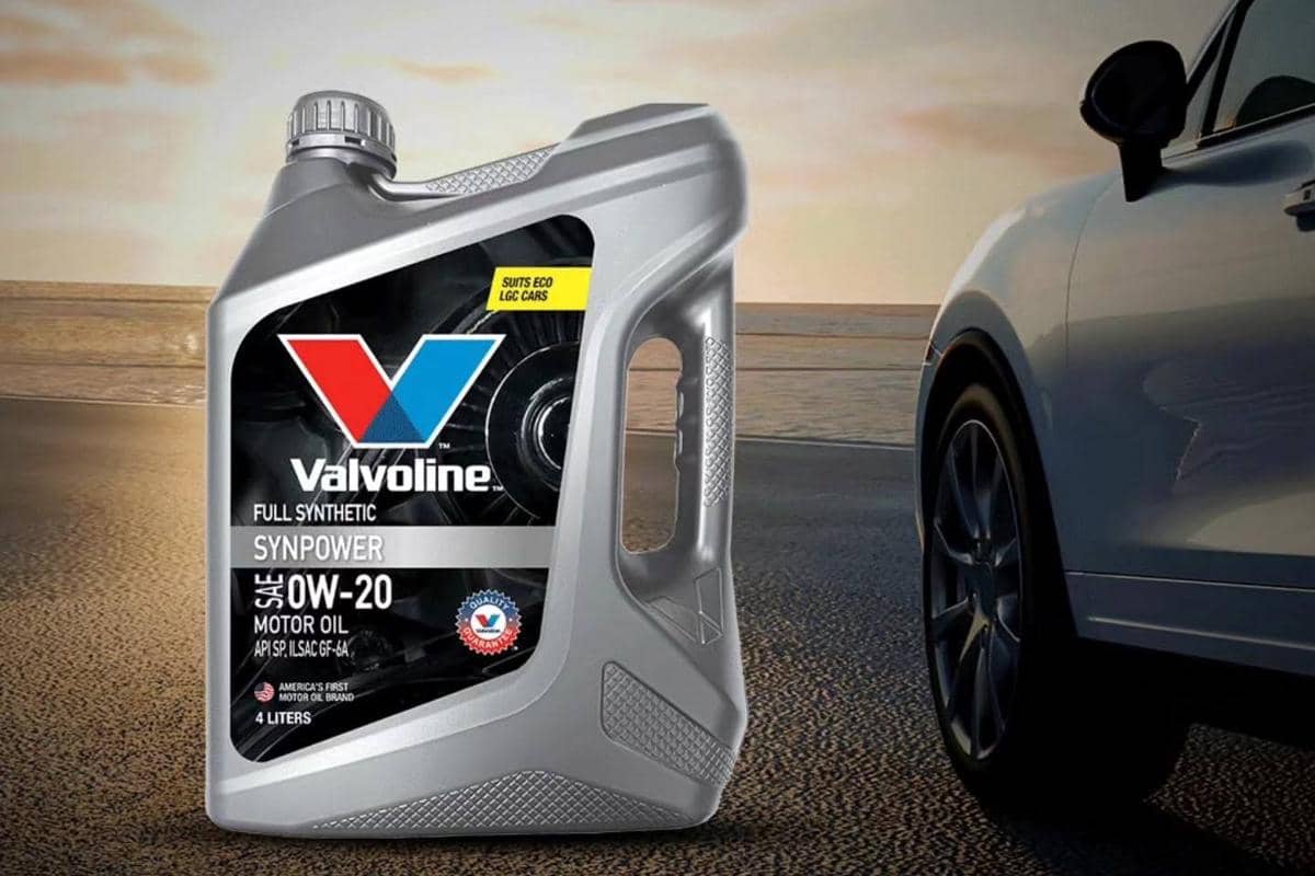 Botol oli mobil Valvoline Full Synthetic SynPower SAE 0W-20 berkapasitas 4 liter berada di samping mobil di tepi jalan saat matahari terbenam.