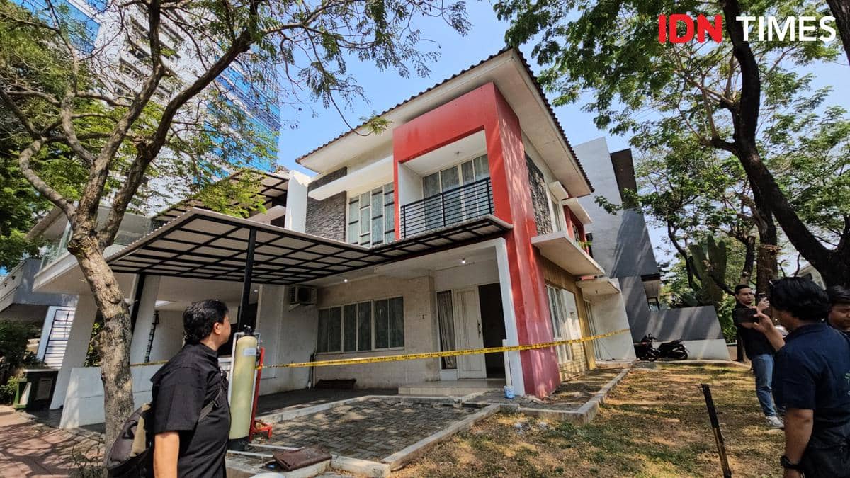 Rumah dua lantai berwarna putih dan merah di kawasan PIK dipasangi garis polisi, dengan beberapa orang berdiri di depannya.