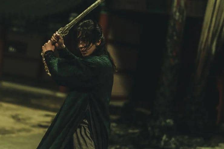 Seorang karakter mengenakan pakaian gelap memegang pedang dengan kedua tangan dalam adegan tegang di drama The East Palace.