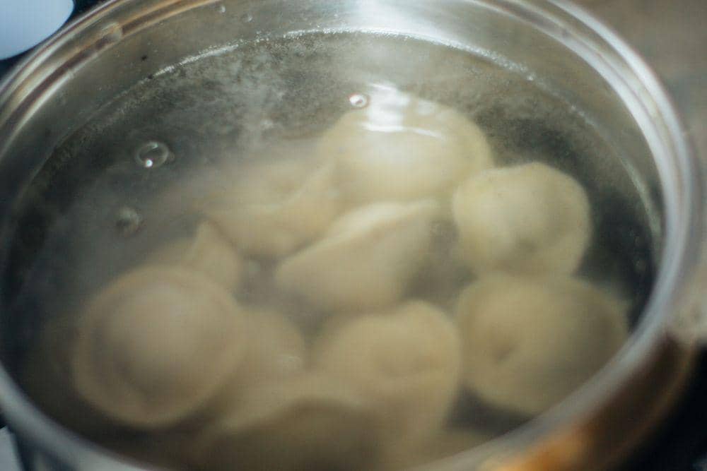 Beberapa potongan pasta sedang direbus dalam air mendidih di dalam panci logam di atas kompor dapur.