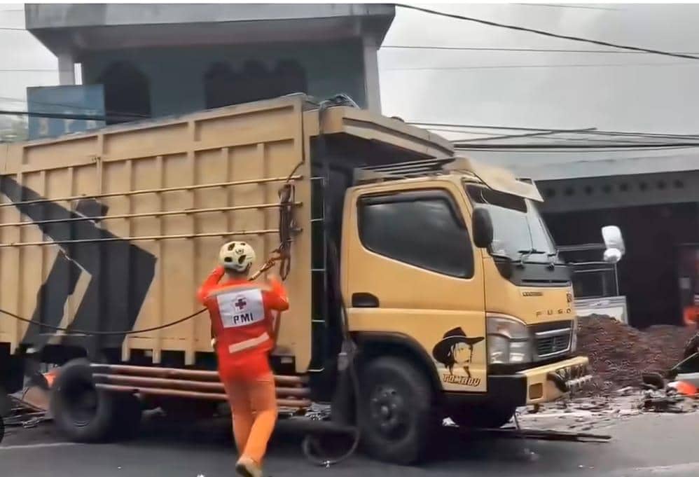 Petugas PMI mengenakan seragam oranye mengevakuasi lokasi kecelakaan truk di Sibolangit dengan kondisi kendaraan rusak parah di jalan raya.