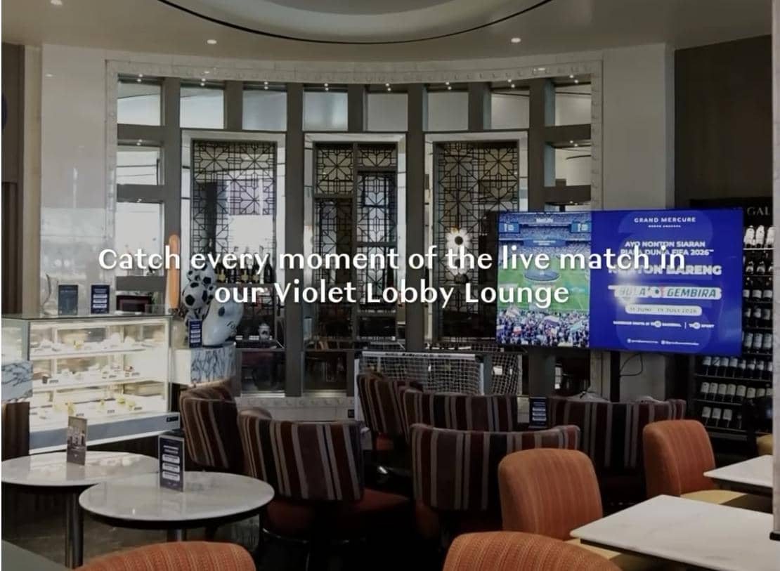Area Violet Lounge di Hotel Grand Mercure Medan dengan kursi bergaris, meja marmer, dan layar besar menayangkan pertandingan langsung.