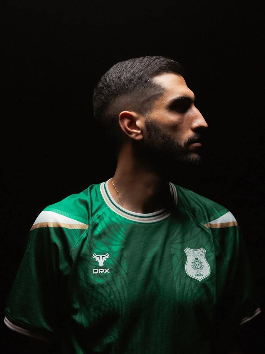 Seorang pria mengenakan jersey hijau PSMS Medan dengan latar belakang gelap, menatap ke arah samping dalam pencahayaan dramatis.