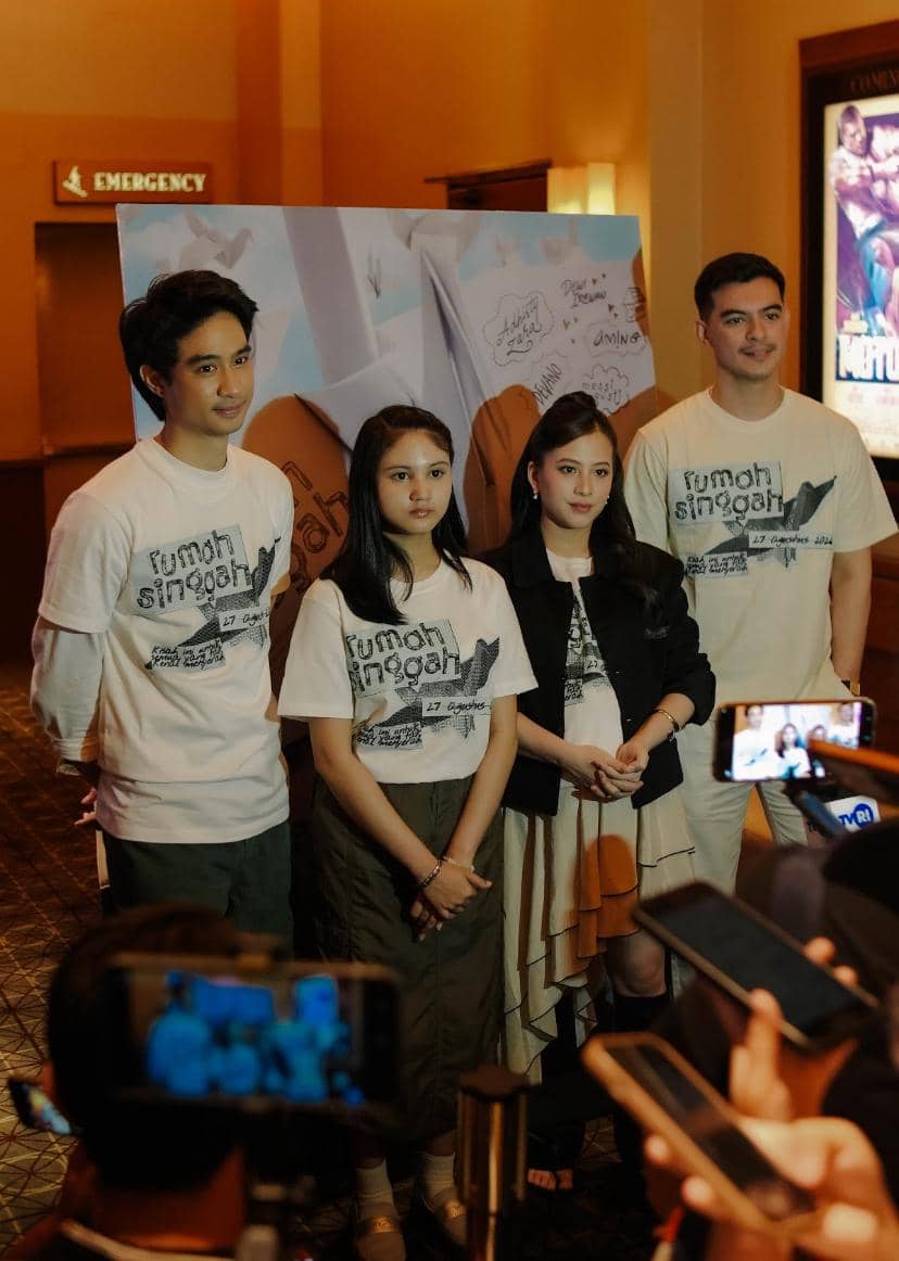 Para pemain film Rumah Singgah berpose di depan poster film saat jumpa pers, mengenakan kaus bertema film yang sama.