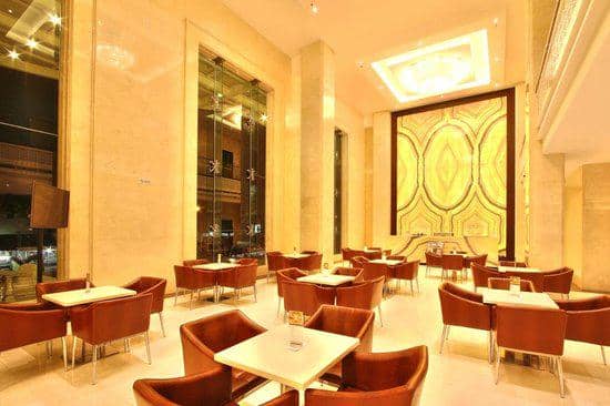 Interior The Onix Lounge dengan pencahayaan hangat, dinding marmer tinggi, meja putih, dan kursi kulit cokelat tertata rapi.
