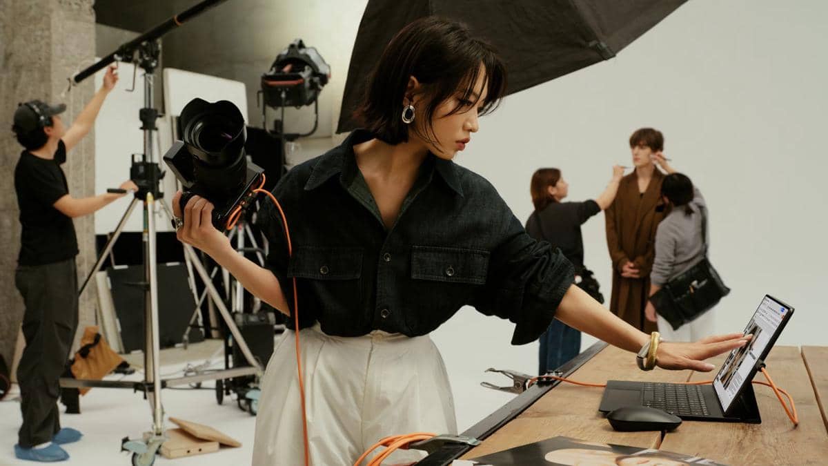Seorang fotografer memegang kamera sambil mengoperasikan tablet HUAWEI MatePad Pro Max di studio pemotretan dengan kru di latar belakang.