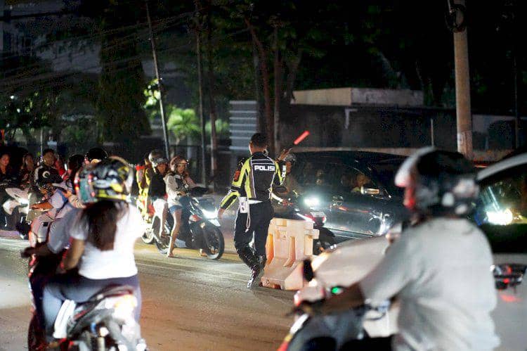 Petugas polisi mengatur lalu lintas dan mengamankan konvoi kendaraan di Kota Kupang saat perayaan Tahun Baru 2026 pada malam hari.