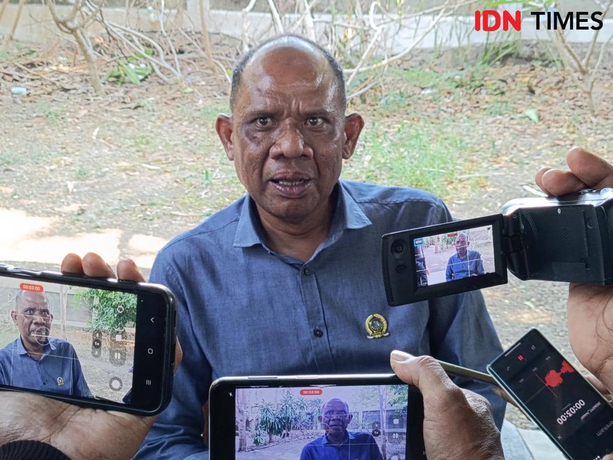 Seorang pria mengenakan kemeja biru sedang diwawancarai oleh beberapa jurnalis yang merekamnya menggunakan ponsel dan kamera.