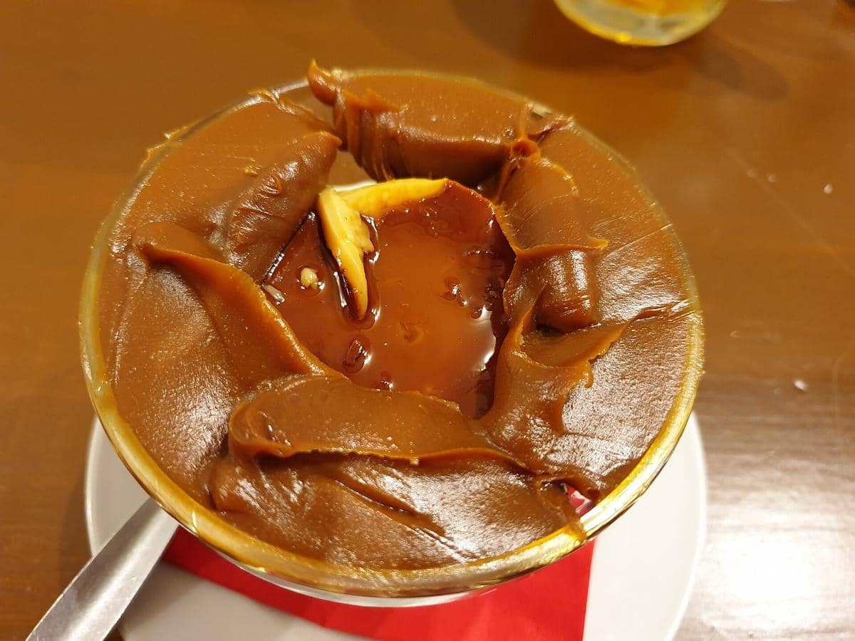 Flan con dulce de leche disajikan dalam mangkuk kaca di atas piring putih dengan alas serbet merah di meja kayu.