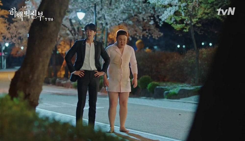 Dua karakter berdiri di jalan malam yang diterangi lampu taman dengan latar pepohonan berbunga dalam cuplikan drama The Bride of Habaek.