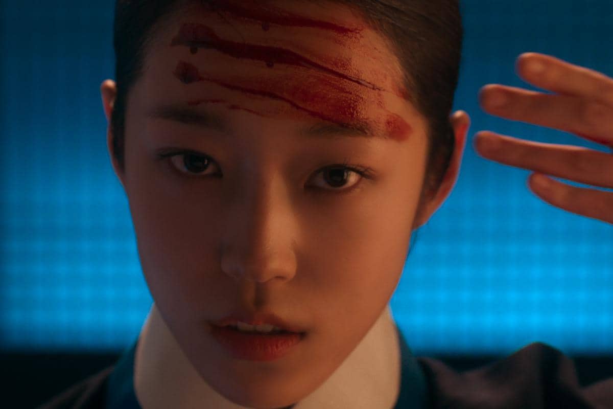 Seorang perempuan dengan luka berdarah di dahi menatap tajam ke depan dalam adegan drama The East Palace berlatar cahaya biru.