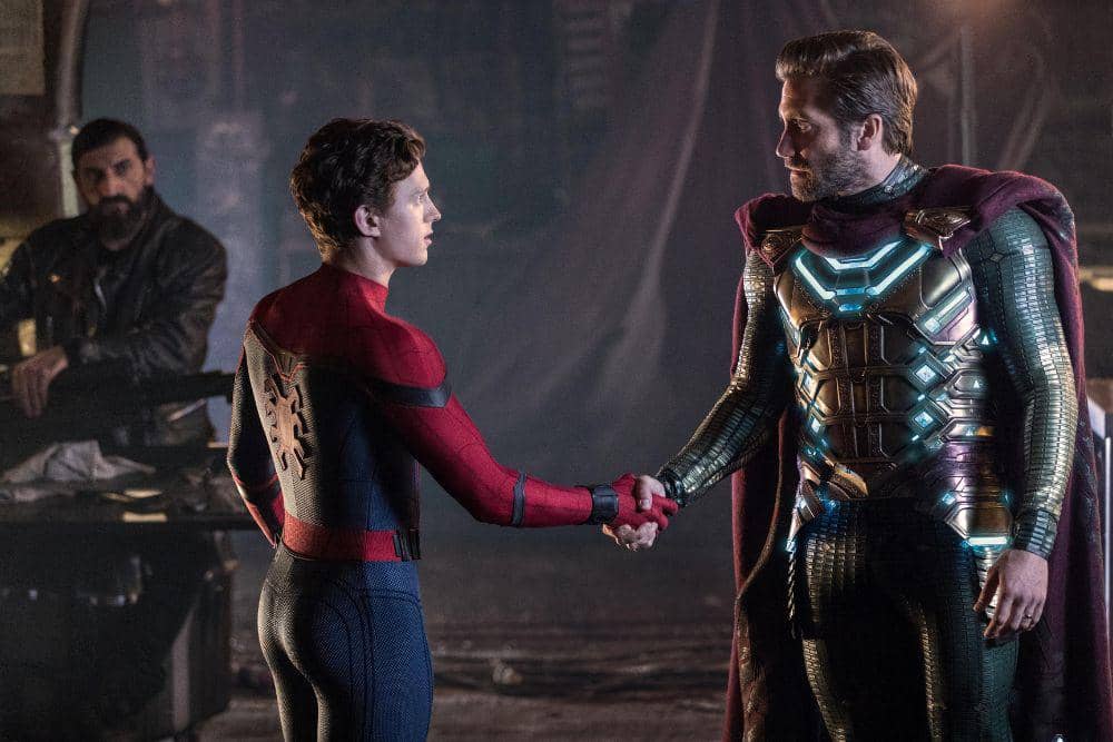 Dua karakter utama dalam kostum superhero berjabat tangan di sebuah ruangan gelap, dengan satu karakter lain duduk di latar belakang.