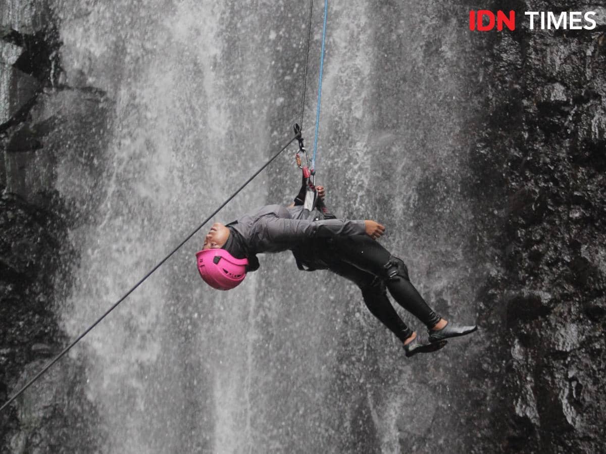 Potret orang sedang rapelling di air terjun