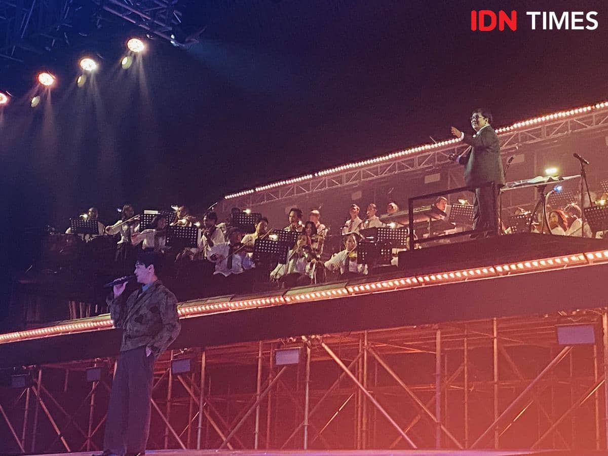 Penyanyi tampil di atas panggung bersama orkestra dan konduktor dalam konser Afgan Retrospektif di Plenary Hall JICC Jakarta.