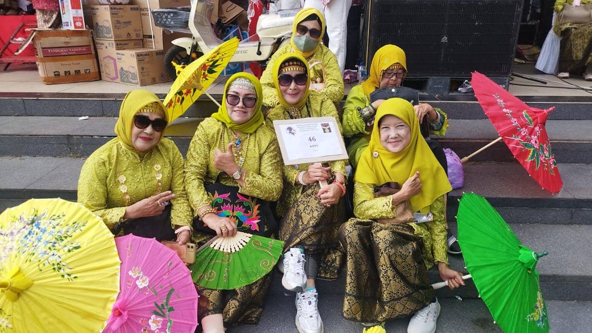 Sekelompok perempuan mengenakan kebaya songket hijau dengan hijab kuning berpose sambil memegang payung warna-warni di acara parade di Palembang.