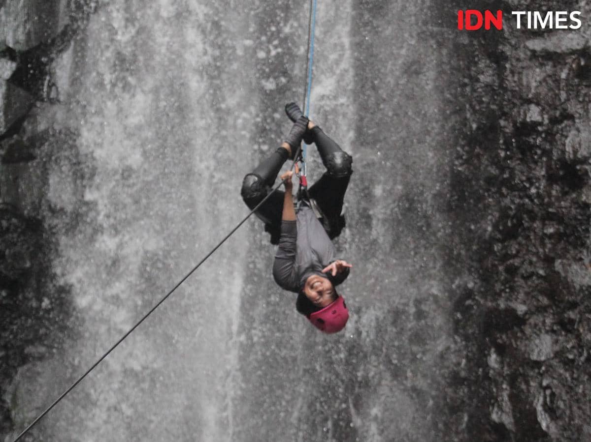 Potret orang sedang rapelling di air terjun