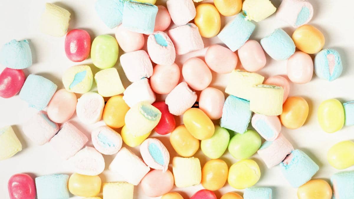 Kumpulan permen warna-warni dan marshmallow kecil dengan berbagai bentuk dan warna pastel di atas permukaan putih.