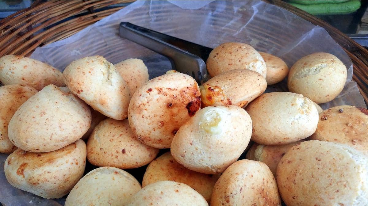 Beberapa potong chipa berwarna keemasan tersusun di atas wadah anyaman dengan latar sendok logam di tengahnya.
