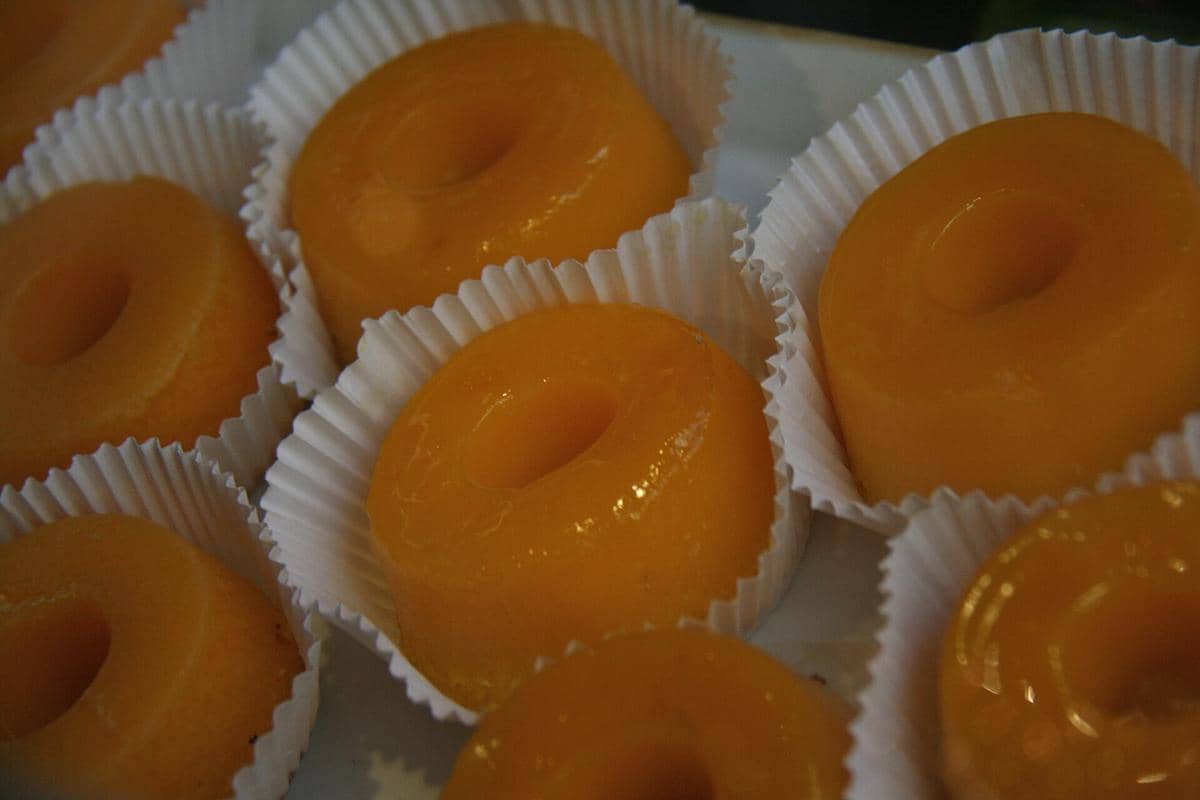 Ilustrasi quindim berwarna kuning keemasan, kue kecil dengan permukaan mengilap dan bentuk membulat.